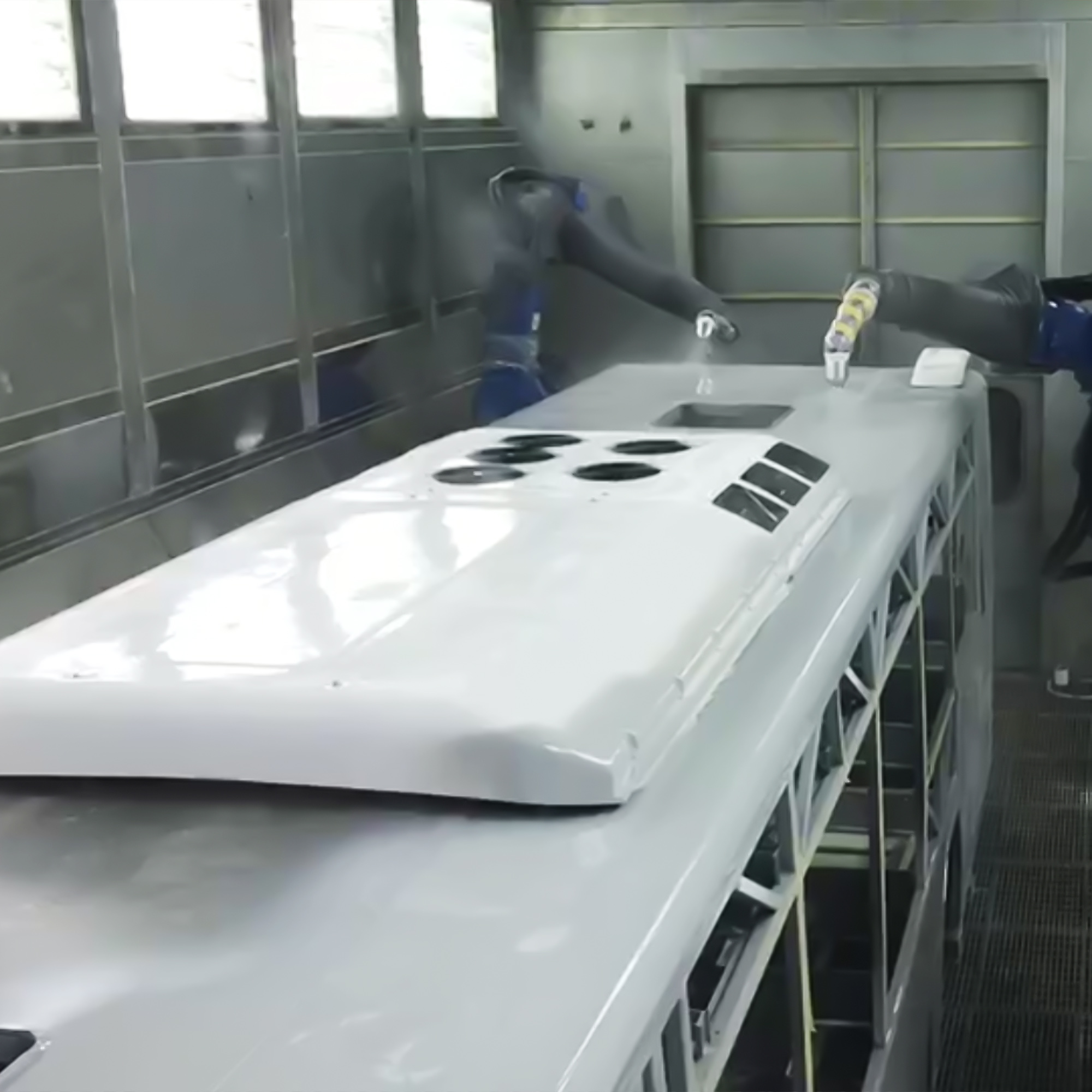 Robotic arm applying coating to a large white bus body panel inside a spray booth